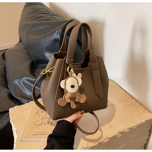 Detail of dark brown lychee leather bucket bag with monkey charm on a stone base