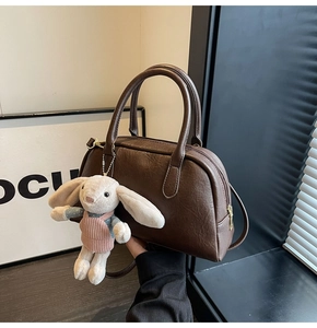 Detail of dark brown Boston bag with lychee texture and cute rabbit plush charm