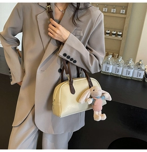 Detail view of a cream Boston bag with brown handles and a cute plush rabbit charm