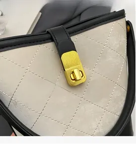 Macro view of beige quilted bucket bag with contrast black trim and gold lock detail