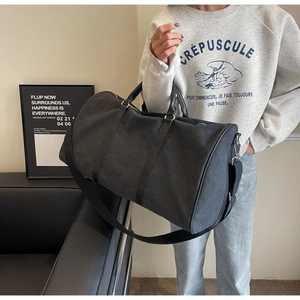 Side view of a large black canvas travel bag being carried by a model in a modern room
