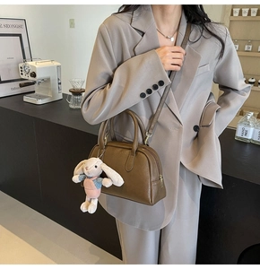 Brown Boston bag with cute rabbit pendant shown on a minimalist cafe background