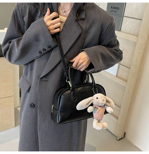 Detail of black matte Boston bag with rabbit charm worn by model in grey coat
