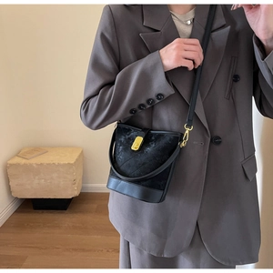 Detail of black quilted bucket bag with gold lock and textured rhombus pattern