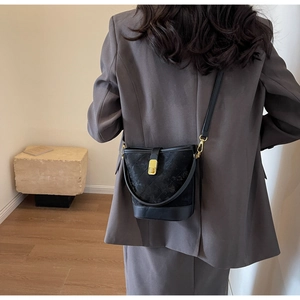 Detail of black quilted bucket bag with gold lock worn over a grey blazer jacket