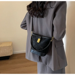 Detail of black quilted bucket bag with gold lock and detachable crossbody strap