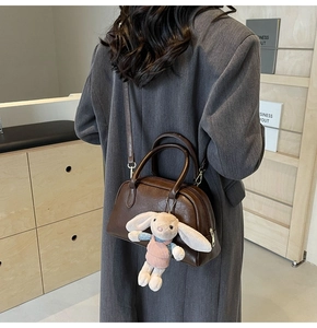Brown leather Boston bag with plush bunny charm shown on model in grey blazer