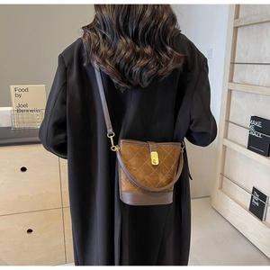 Detail of brown quilted suede bucket bag with gold twist lock worn as a crossbody bag
