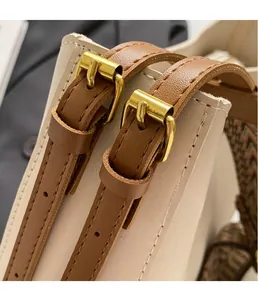 Detail van de gouden metalen gesp en stiksels op de schouderriem van de beige emmer tas