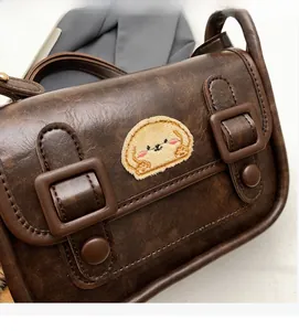 Détail de la sacoche vintage marron avec broderie de chien et sangles à boucles