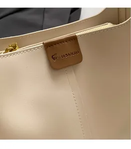 Detail van OUMABAOLUO merklogo op crèmewitte leren tas met gouden metalen ritssluiting
