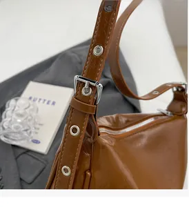 Close-up of caramel leather shoulder bag showing glossy finish and silver metal eyelets