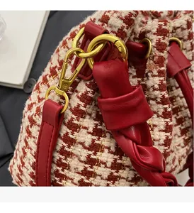 Détail du tissu pied-de-poule aux fils dorés et poignée en cuir rouge du sac seau