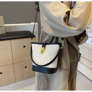Quilted bucket bag in black and white leather with gold lock shown on a beige trench coat