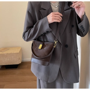 Detail of dark brown quilted bucket bag with gold hardware on a gray blazer