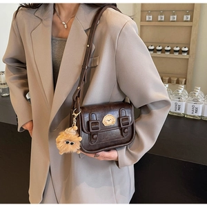 Détail du sac bandoulière marron vintage avec broderie chiot et breloque en peluche sur veste