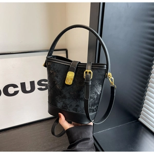 Detail of black quilted bucket bag with gold metal clasp and adjustable shoulder strap