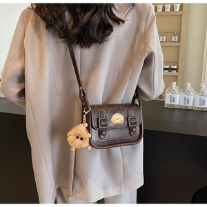 Détail du sac bandoulière vintage marron foncé avec écusson d'ours et breloque en peluche