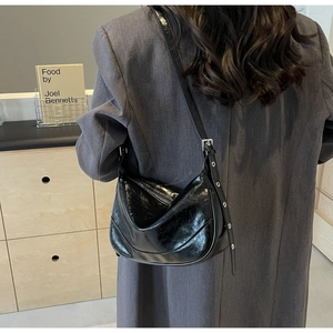 Detail of adjustable strap and glossy pleated leather texture on black underarm bag