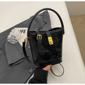 Detail of black quilted bucket bag featuring gold metal clasp and adjustable strap