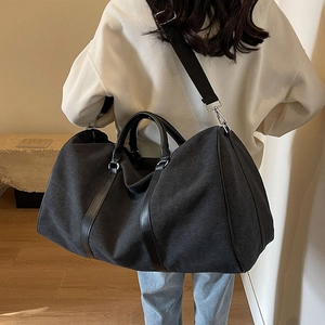 Large black canvas travel bag with leather trim and shoulder strap shown on a model