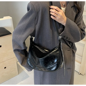 Detail of black glossy patent leather shoulder bag with vintage texture and adjustable strap