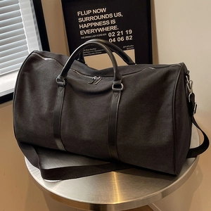 Large black canvas travel bag with leather handles and adjustable shoulder strap for trips
