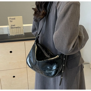 Detail of black glossy crescent bag with silver eyelet strap and fine leather texture