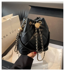 Close-up of black quilted bucket bag with gold chain strap and spherical charm detail