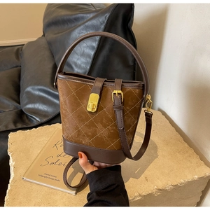 Detail of a brown suede bucket bag with quilted patterns and a golden twist lock