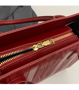 Détail macro de la fermeture éclair dorée sur le sac en cuir rouge à texture ondulée