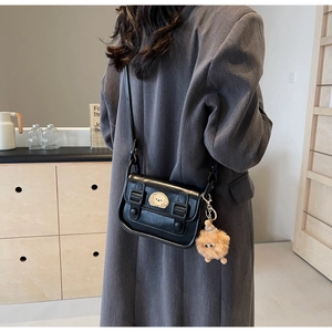 Détail d'un sac bandoulière vintage noir avec double boucles et breloque peluche monstre