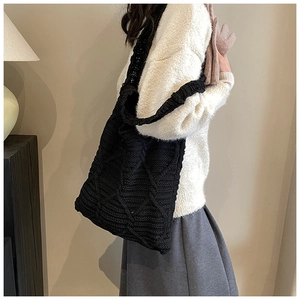 Dettaglio della borsa tote in maglia nera con motivo a rombi indossata sulla spalla