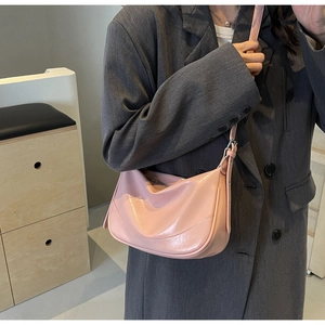 Close-up of pink glossy leather hobo bag worn by a model in a minimalist setting