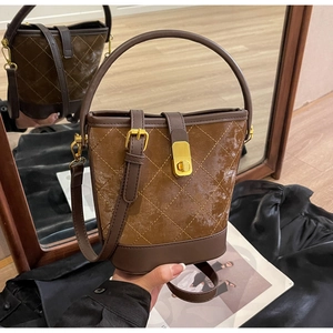 Detail of a brown quilted bucket bag with gold lock hardware and versatile straps