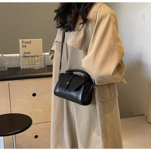 Detail of a black crossbody handbag with flap closure and adjustable shoulder strap on a model