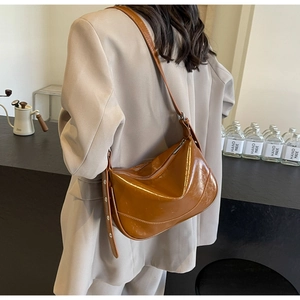 Detail of a brown glossy patent leather hobo shoulder bag with metal zipper and wide strap