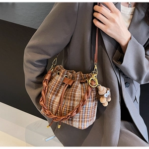 Détail du sac seau en tweed à carreaux avec poignée tressée, bandoulière et bijou en peluche