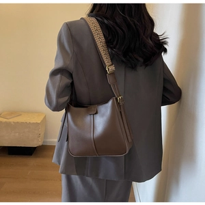 Detail of a dark brown leather bucket bag featuring a geometric woven wide shoulder strap