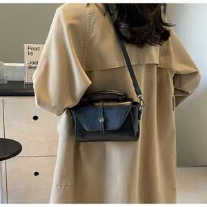 Black leather crossbody bag styled with a trench coat in a cozy indoor setting