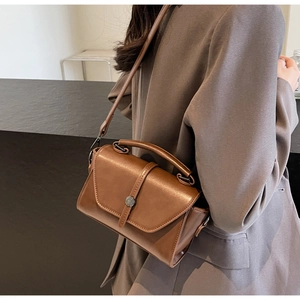 Brown retro leather handbag with metal buckle worn over a grey blazer detail view