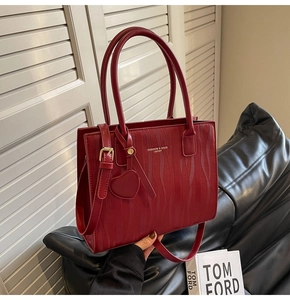 Détail du sac cabas en cuir rouge texturé avec breloque cœur et logo de mode
