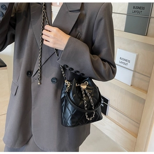 Detail of black quilted bucket bag with gold chain strap on a grey suit outfit
