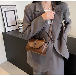 Close-up of vintage brown leather handbag with metal buckle worn by a model in a modern room