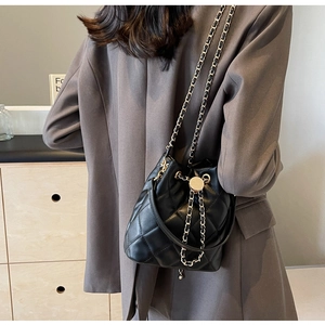 Detail of black quilted bucket bag with chain strap and gold hardware on model