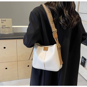 Detailed shot of chic cream bucket bag with wide woven strap and brown leather accents