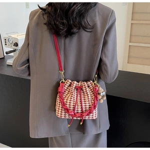 Sac seau en pied-de-poule rouge avec bandoulière en cuir et charm sur un mannequin