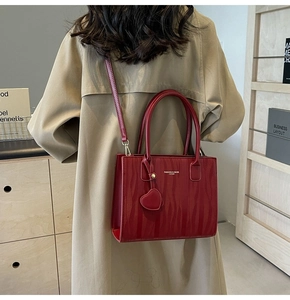 Sac de mariée rouge avec texture ondulée et breloque cœur porté sur un trench-coat kaki