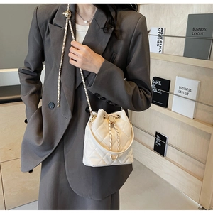 Detail of white quilted bucket bag with gold chain strap worn on grey blazer