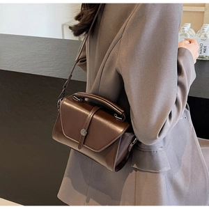 Model wearing dark brown leather crossbody bag with silver buckle over a grey blazer